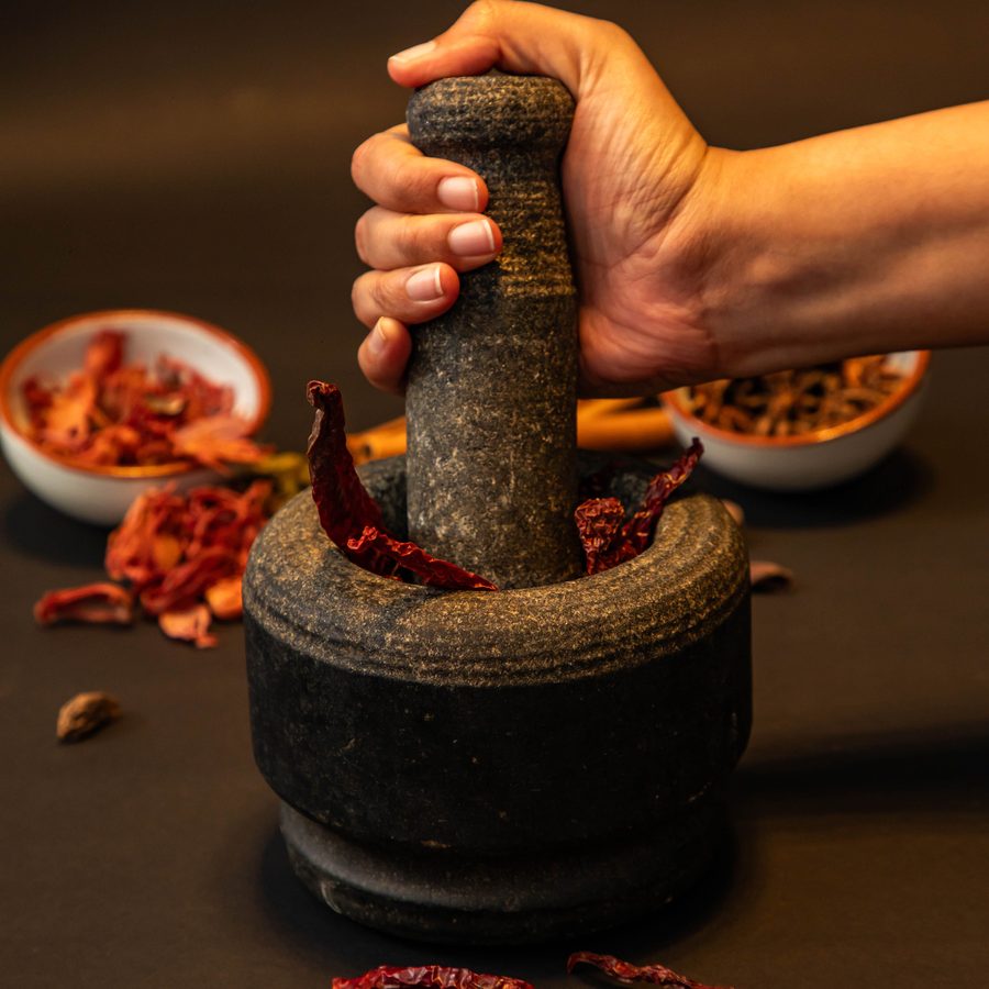 Hand grinding dried red chillies in a traditional stone mortar for fresh masala