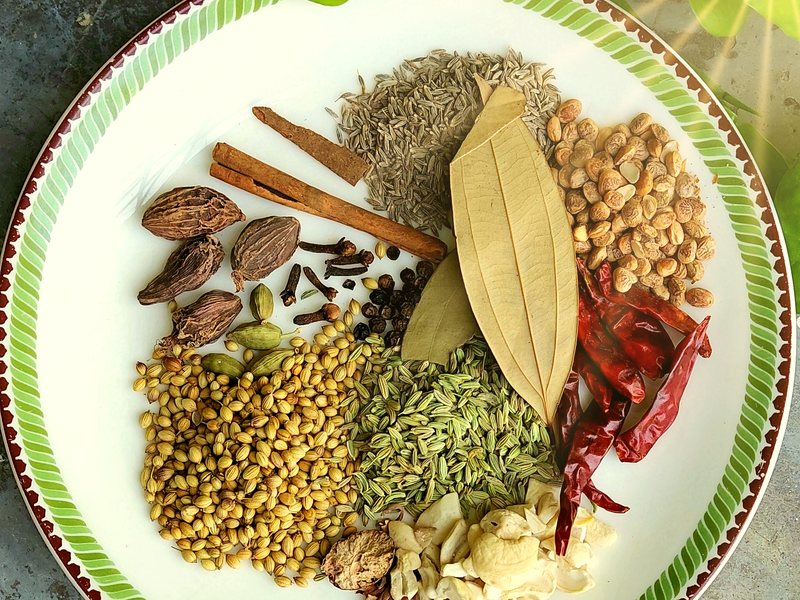 Whole spices for masala – cardamom, cinnamon, cumin, coriander, fennel, chillies and bay leaf in sunlight